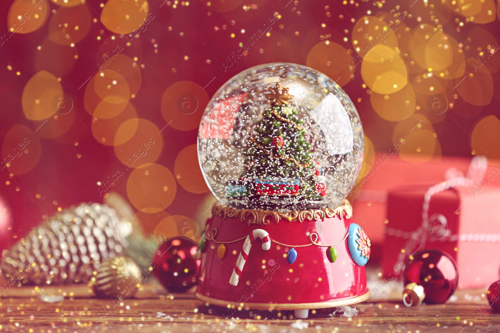 Image of Beautiful snow globe with Christmas tree on wooden table against red background. Bokeh effect