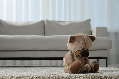 Cute lonely teddy bear on floor near sofa in room. Space for text