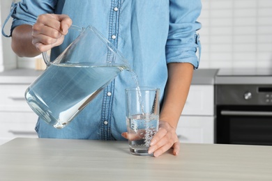 Photo of Woman pouring water into glass at table, closeup