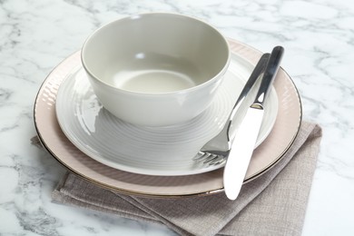 Clean plates, bowl, cutlery and napkin on white marble table, closeup