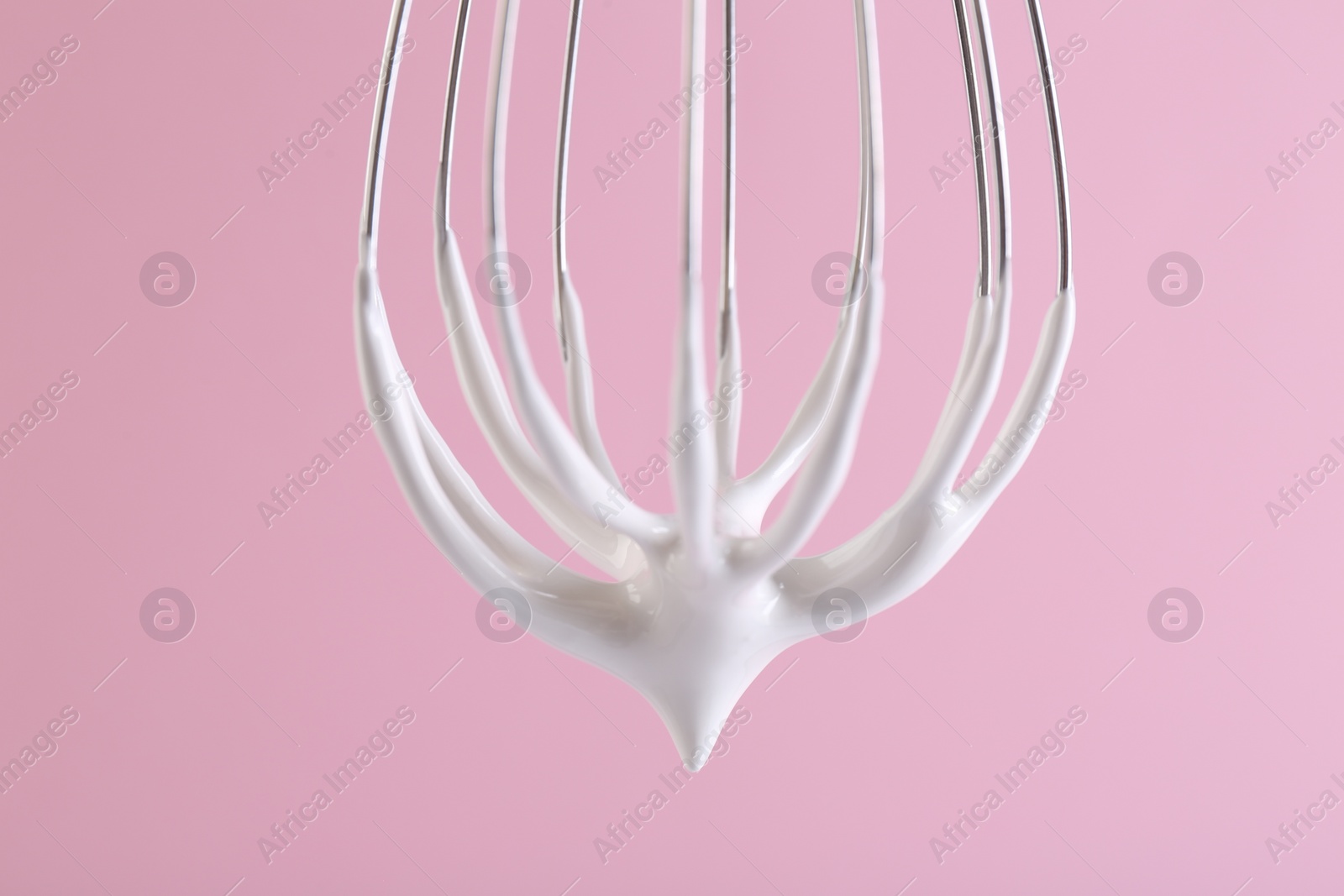 Photo of Whisk with whipped cream on pink background, closeup