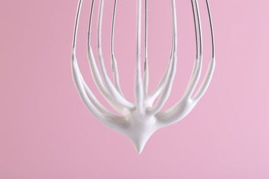 Photo of Whisk with whipped cream on pink background, closeup
