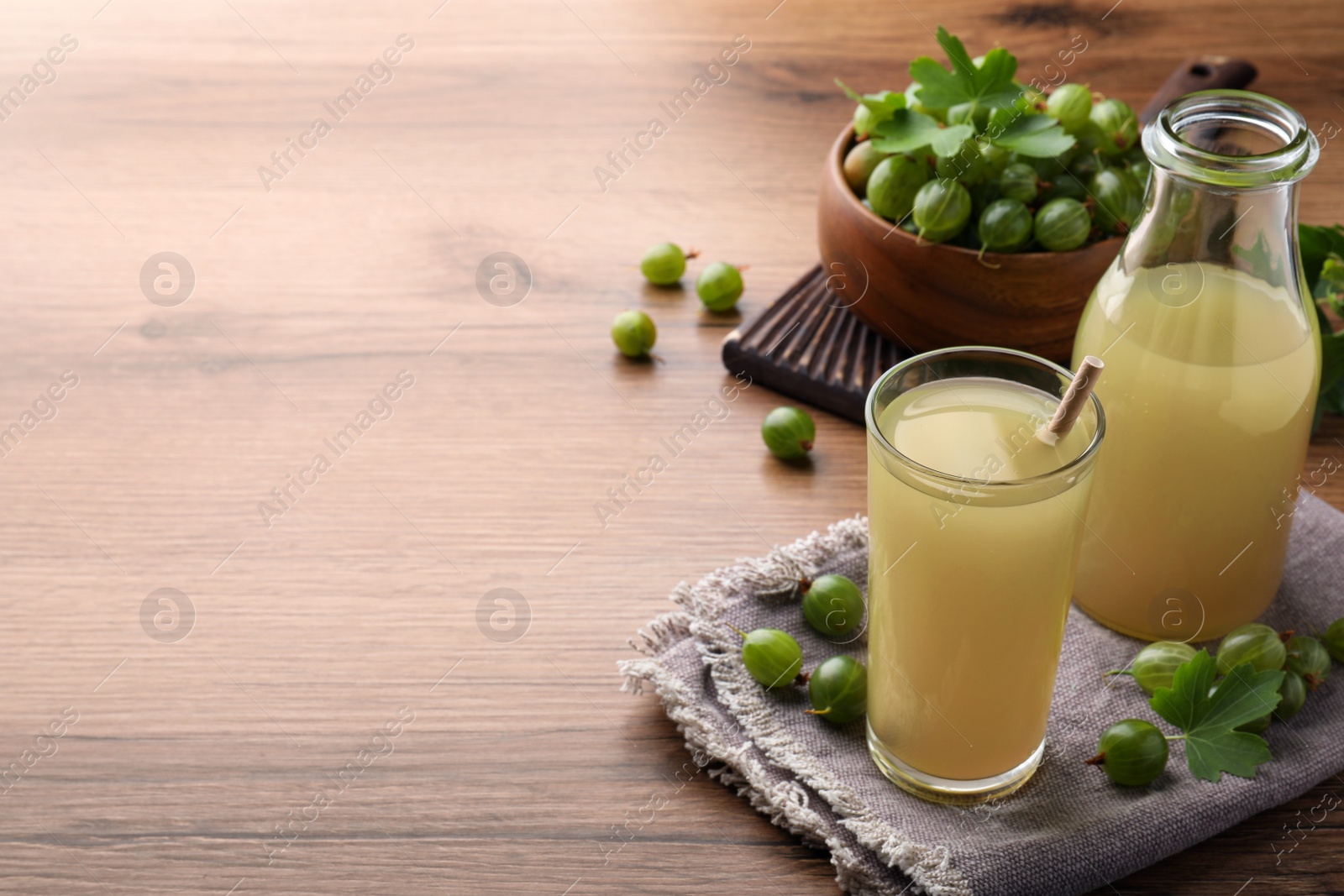 Photo of Tasty gooseberry juice on wooden table. Space for text