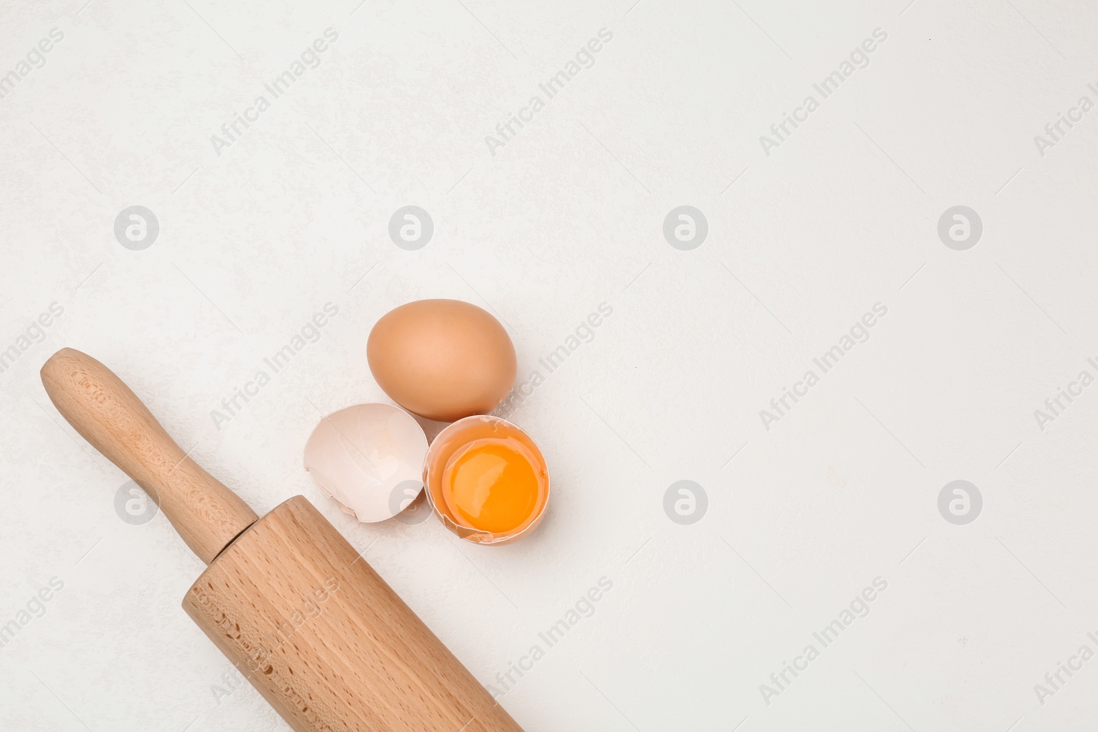 Photo of Raw eggs and rolling pin on white table, top view with space for text. Baking pie