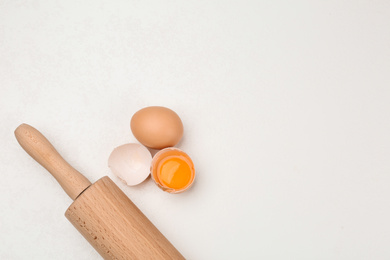 Raw eggs and rolling pin on white table, top view with space for text. Baking pie