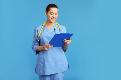 Photo of Portrait of young medical assistant with stethoscope and clipboard on color background. Space for text