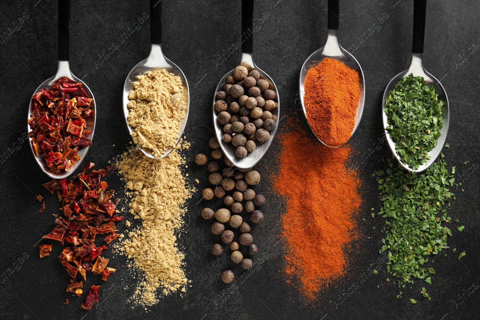 Photo of Metal spoons with different spices on black table, flat lay