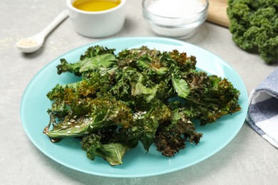 Photo of Tasty baked kale chips on light grey table, closeup