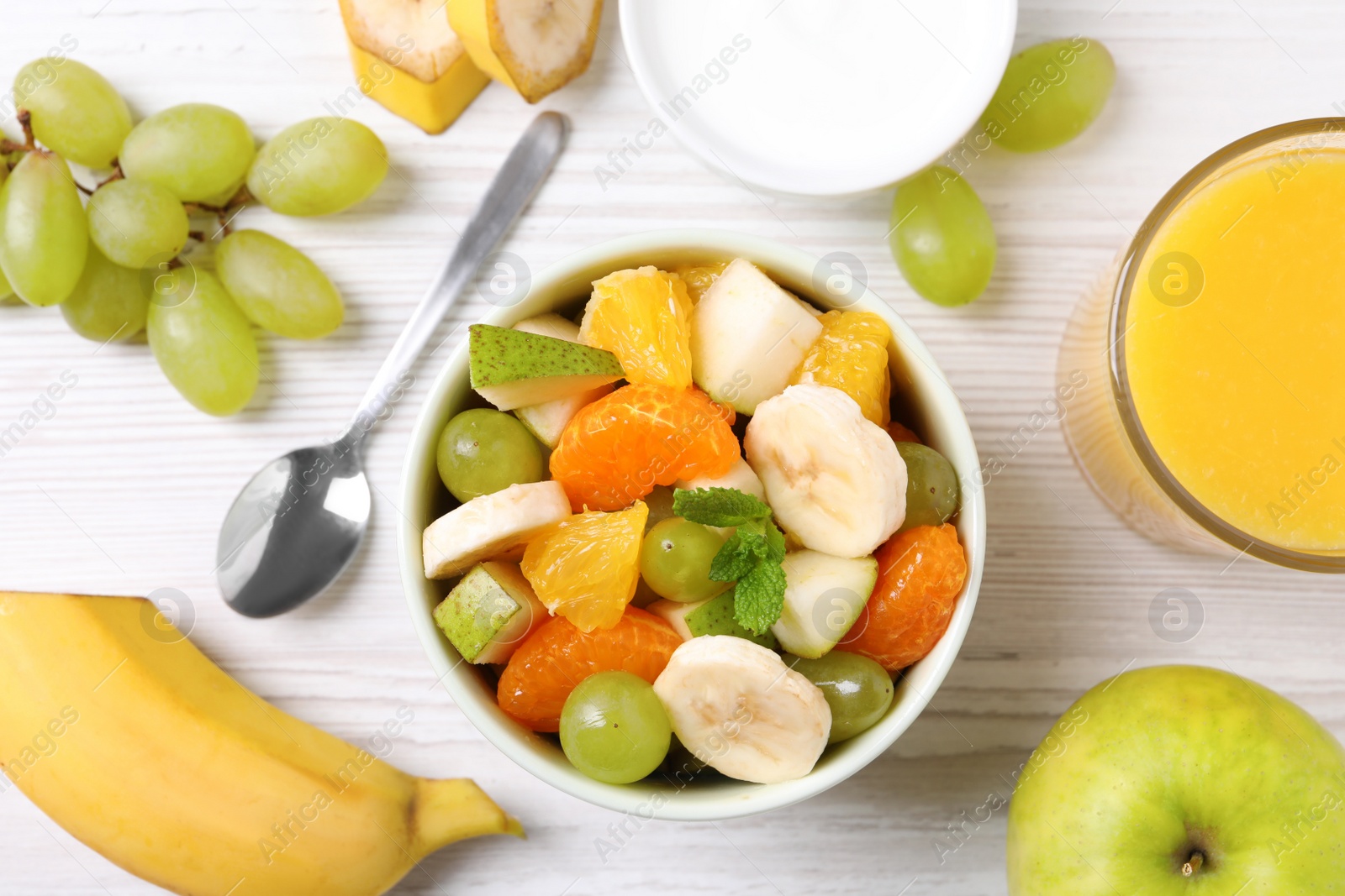 Photo of Delicious fresh fruit salad in bowl on white wooden table, flat lay