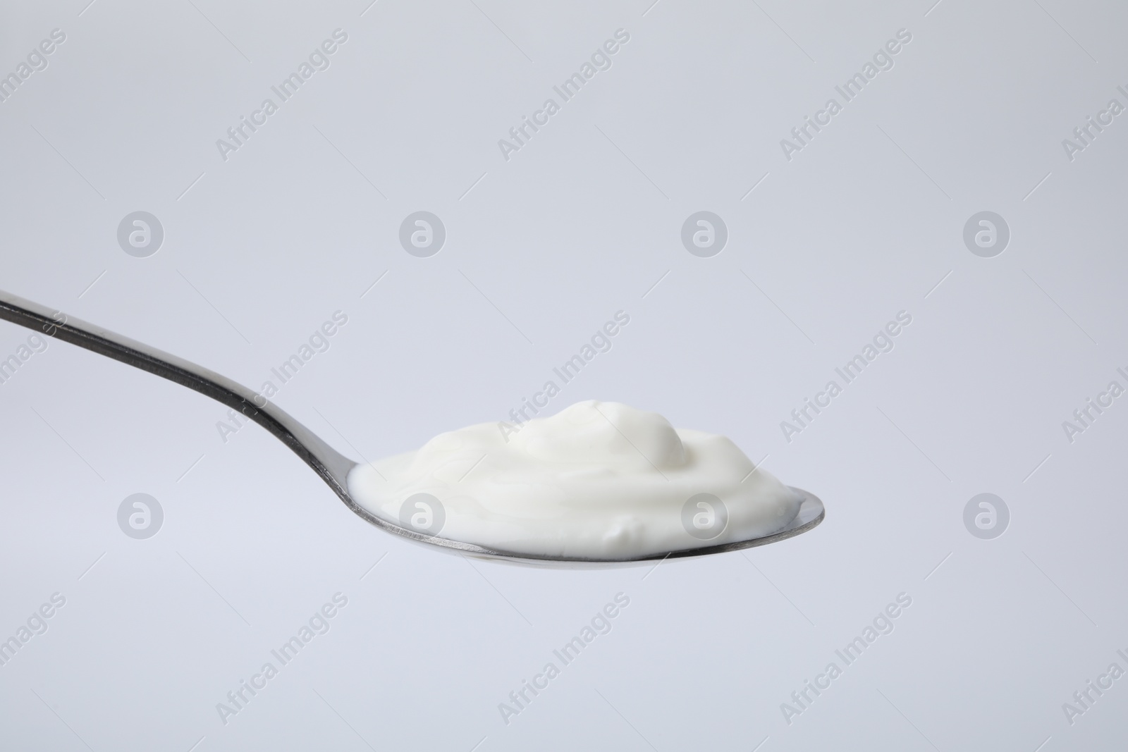 Photo of Delicious natural yogurt in spoon on light background