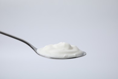 Delicious natural yogurt in spoon on light background