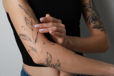 Woman applying cream on her arm with tattoos against light background, closeup