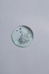 Photo of Drop of cosmetic serum on white background, top view