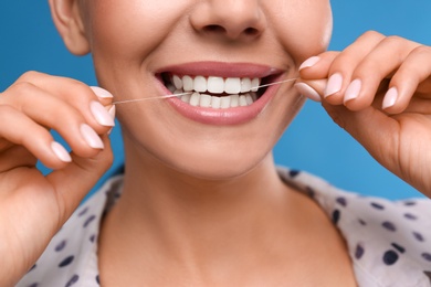 Photo of Young woman flossing her teeth on blue background, closeup. Cosmetic dentistry