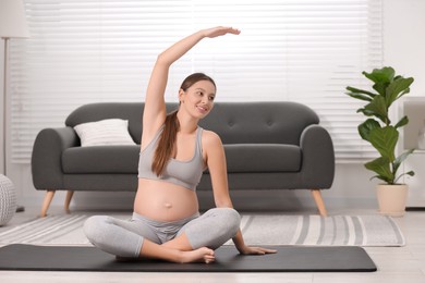 Pregnant woman doing exercises on yoga mat at home