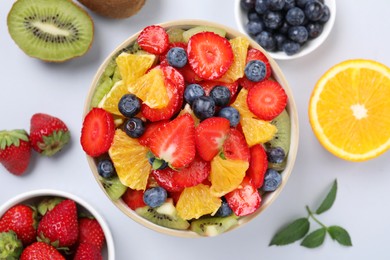 Yummy fruit salad in bowl and ingredients on light background, flat lay
