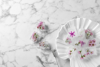 Photo of Flat lay composition with floral ice cubes on marble background. Space for text