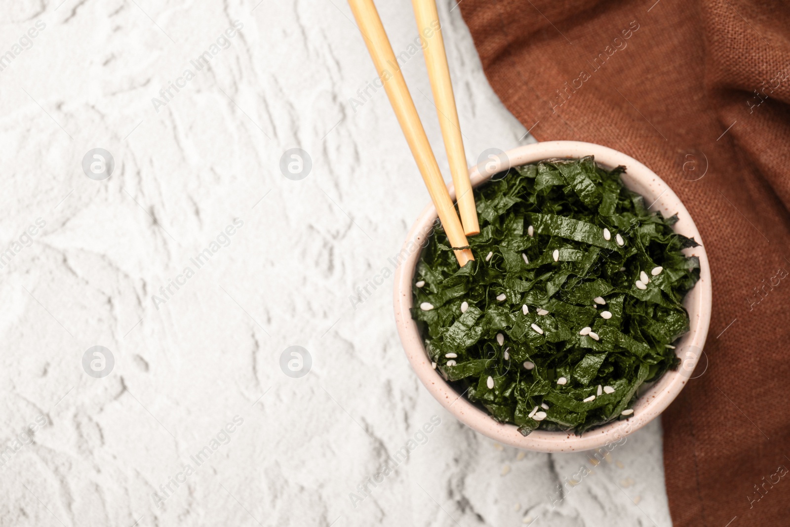 Photo of Chopped nori sheets with sesame and chopsticks on white textured table, flat lay. Space for text