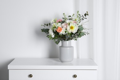 Bouquet with beautiful flowers on white chest of drawers indoors
