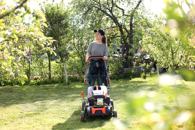 Photo of Smiling woman cutting green grass with lawn mower in garden