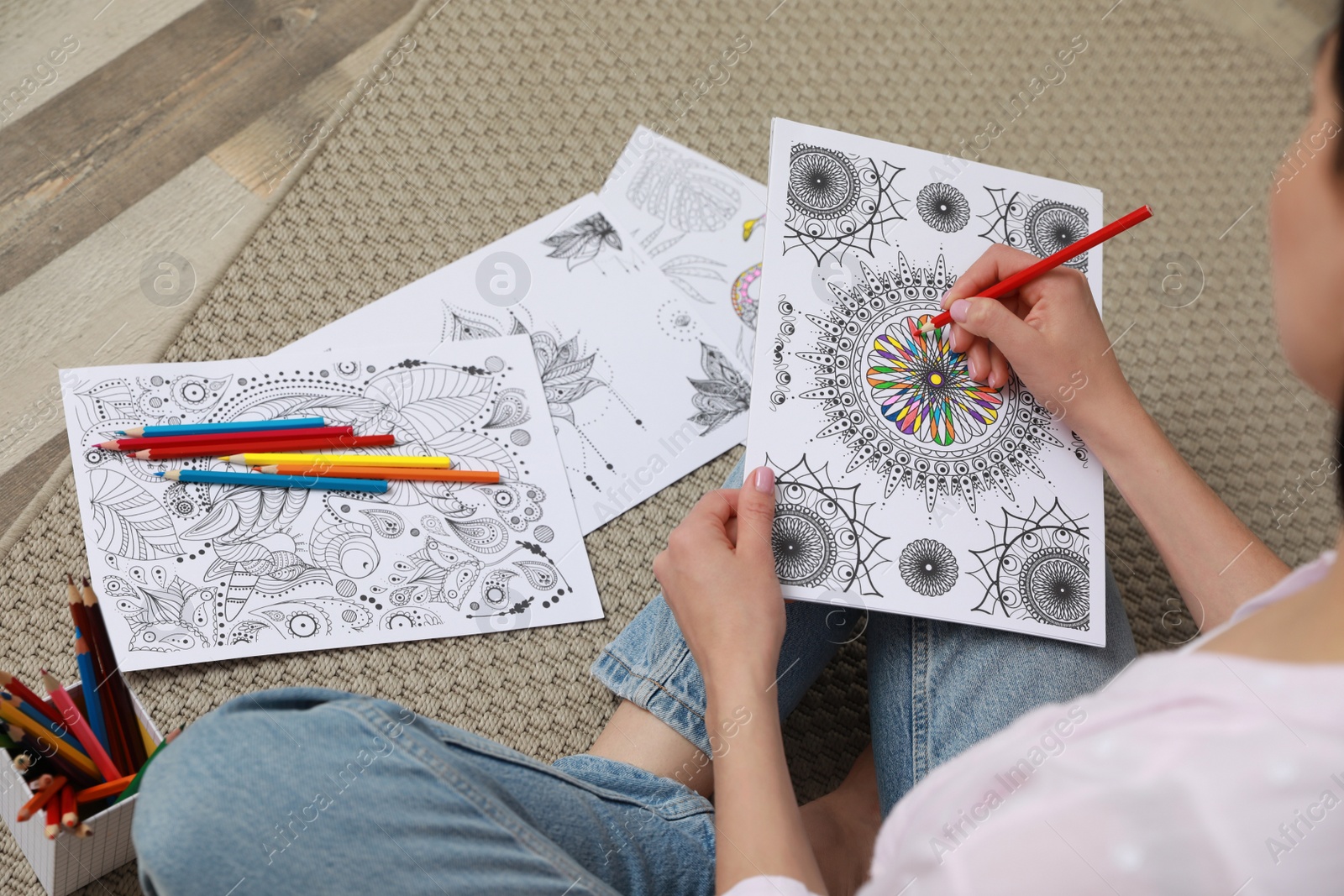 Photo of Young woman coloring antistress page on floor, closeup