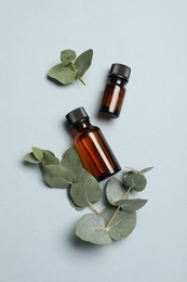 Aromatherapy. Bottles of essential oil and eucalyptus leaves on light grey background, flat lay