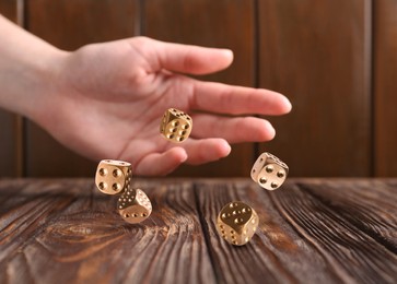 Woman throwing golden dice on wooden table, closeup