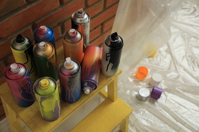 Photo of Used cans of spray paints on stand near brick wall indoors. Graffiti supplies