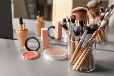 Set of professional brushes and makeup products near mirror on grey table, space for text
