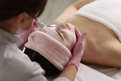 Cosmetologist applying mask on woman's face, closeup