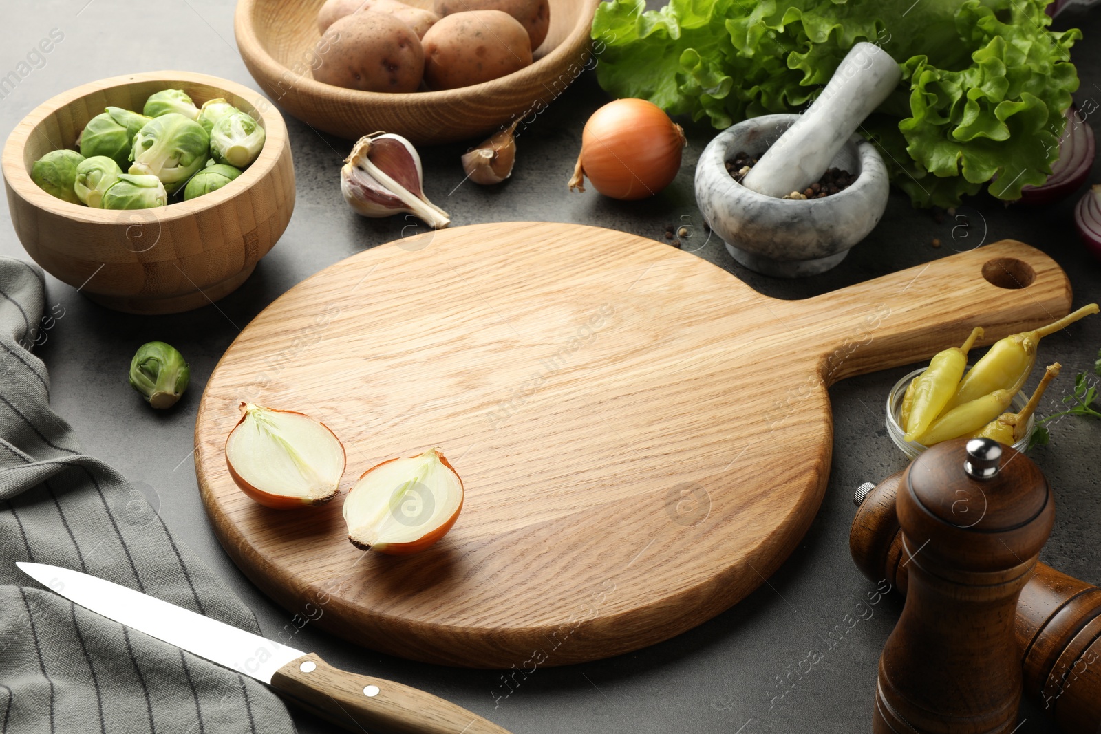 Photo of Wooden cutting board and products on dark textured table, closeup