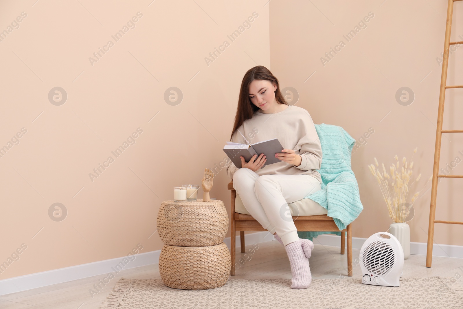 Photo of Woman reading book near modern electric fan heater indoors, space for text