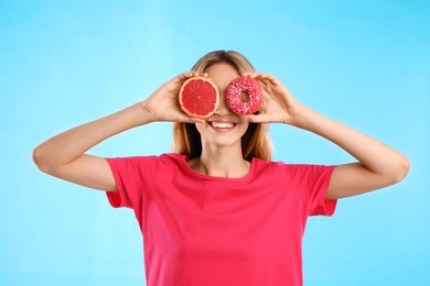 Photo of Woman choosing between doughnut and healthy grapefruit on light blue background