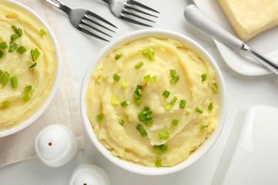 Bowls of delicious mashed potato with green onion on white table, flat lay