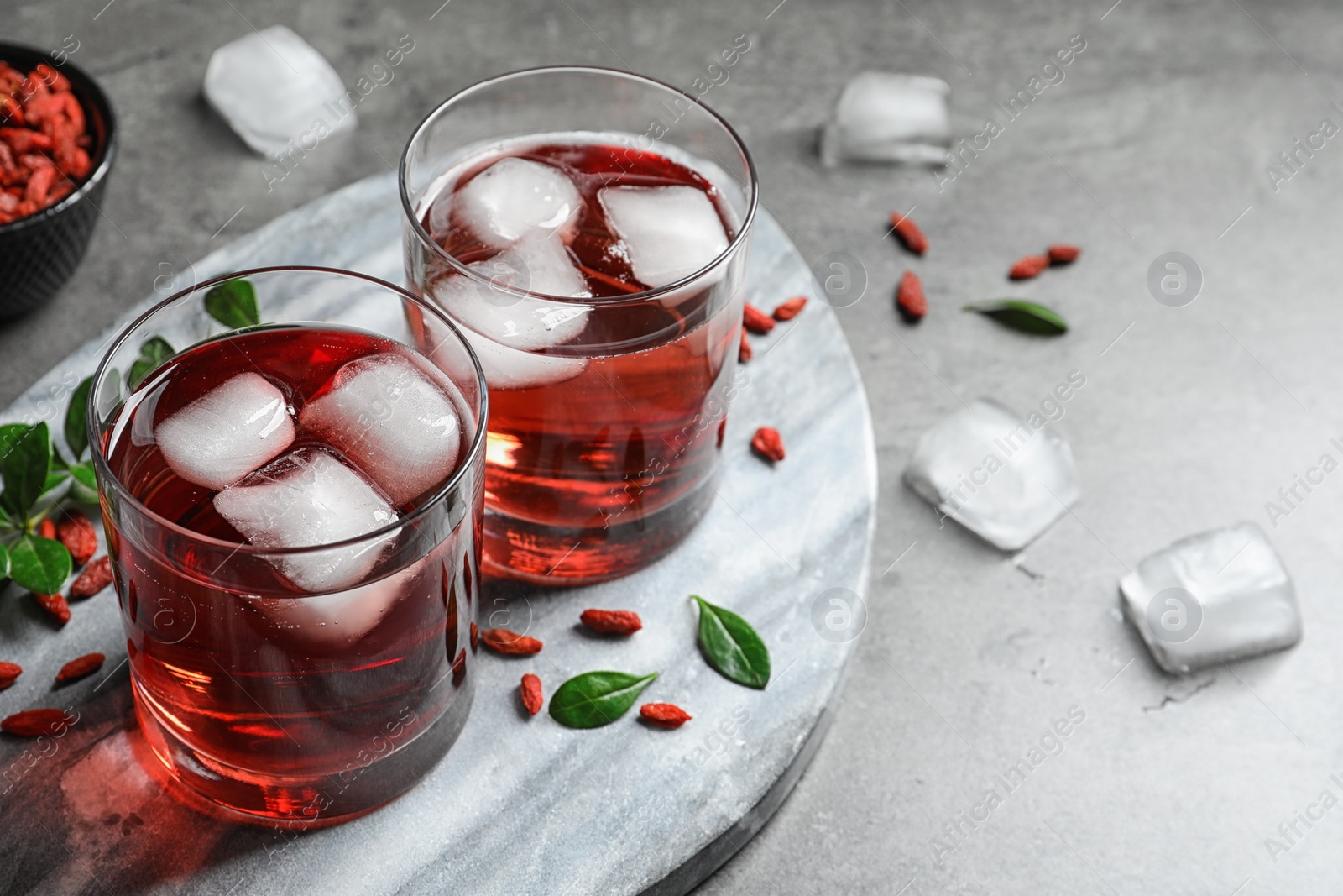 Photo of Healthy goji juice with ice in glasses on grey table. Space or text