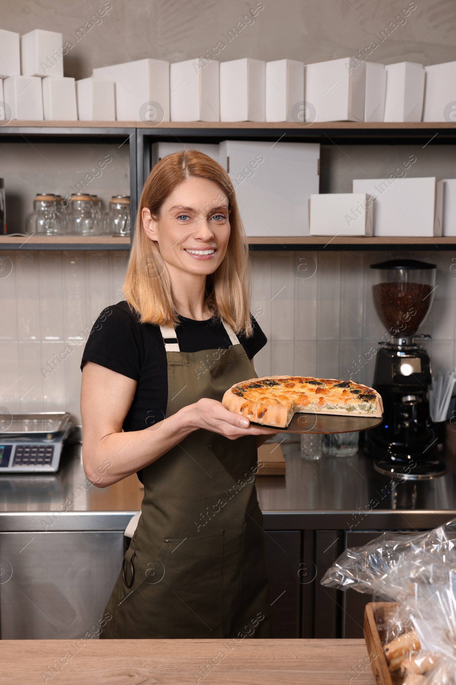 Photo of Happy seller holding delicious quiche at cashier desk in bakery shop