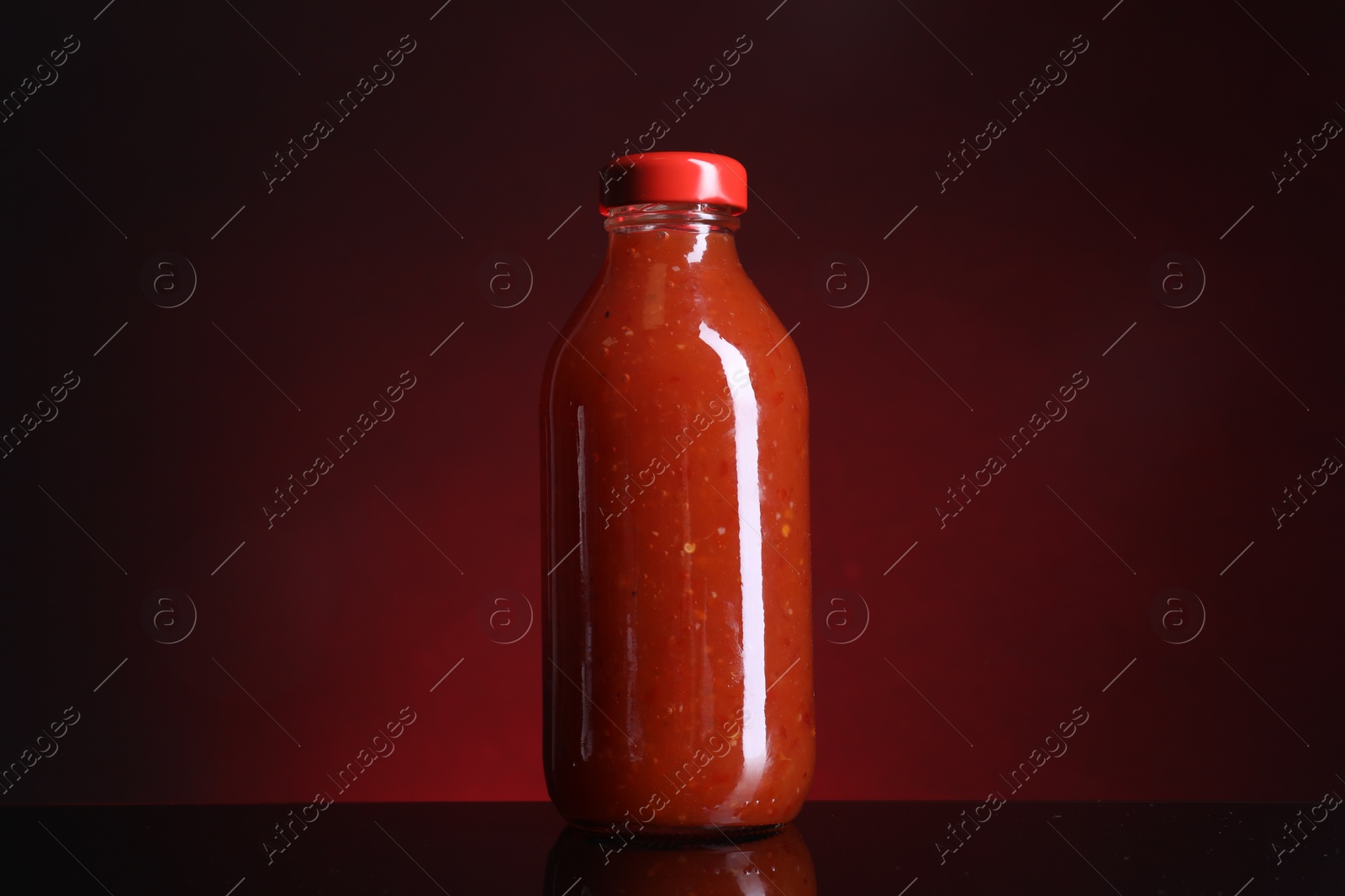 Photo of Spicy chili sauce in bottle on against dark background