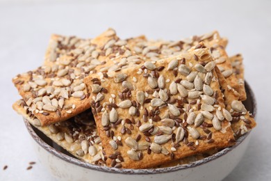 Photo of Cereal crackers with flax, sunflower and sesame seeds in bowl on light table, closeup