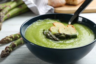 Photo of Delicious asparagus soup in bowl on white wooden table, closeup