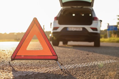 Photo of Warning triangle and broken car on roadside, selective focus