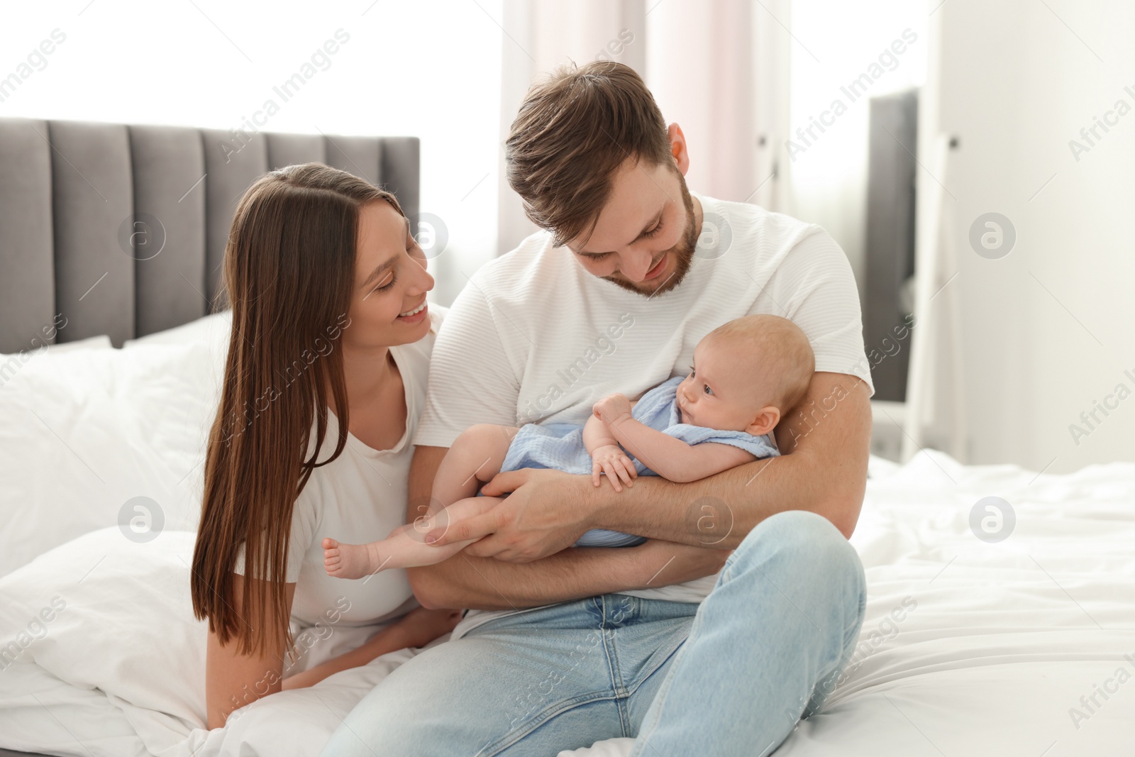 Photo of Happy family. Parents with their cute baby on bed indoors