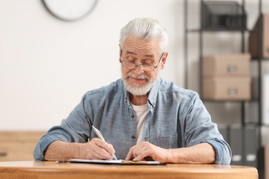 Photo of Senior man signing Last Will and Testament at table indoors