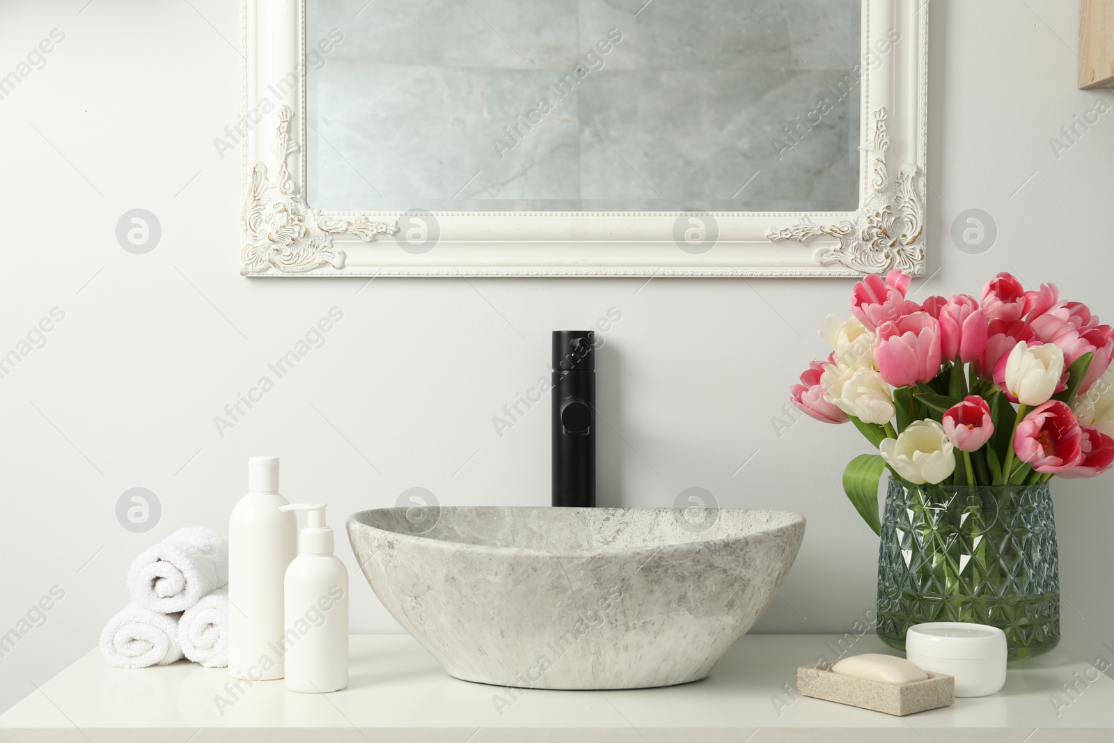 Photo of Vase with beautiful pink tulips and toiletries near sink in bathroom