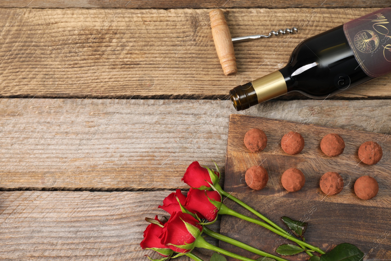 Photo of Bottle of red wine, chocolate truffles, corkscrew and roses on wooden table, flat lay. Space for text