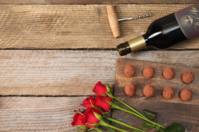 Photo of Bottlered wine, chocolate truffles, corkscrew and roses on wooden table, flat lay. Space for text