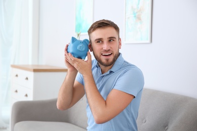 Photo of Young man with piggy bank on sofa in living room