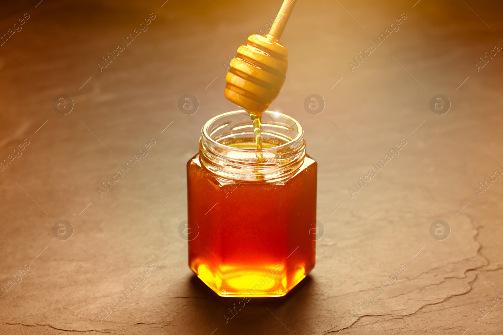 Image of Natural honey dripping from dipper into glass jar on table under sunlight