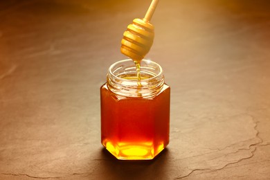 Natural honey dripping from dipper into glass jar on table under sunlight