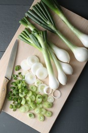 Photo of Board with knife, whole and cut spring onions on grey wooden table, flat lay