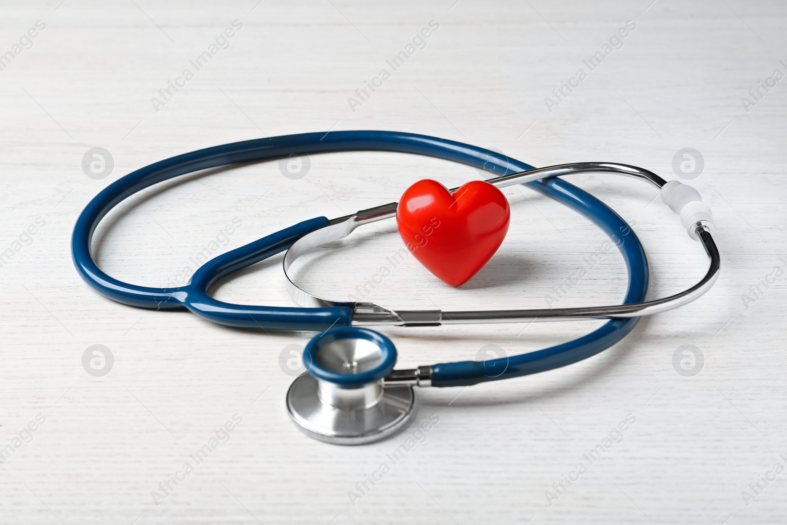 Photo of Stethoscope and red heart on white wooden table. Cardiology concept